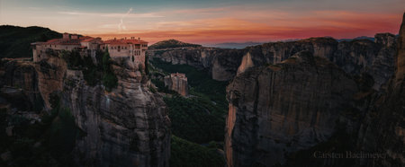 A panoramic view of a cliffside village during sunset, with buildings perched on rocky outcrops and surrounded by lush greenery.の写真素材
