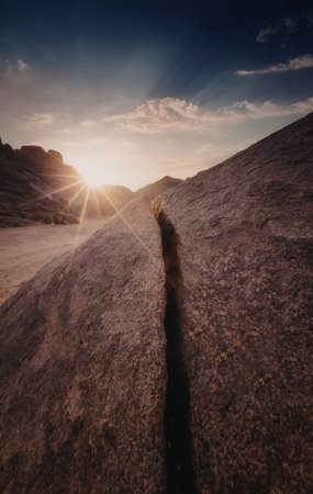 A serene sunrise over rugged, rocky terrain with a prominent crack running through the rocks,...