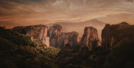 A breathtaking sunset casts a warm glow over a landscape of towering rock formations surrounded by lush greenery.の写真素材