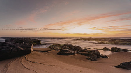 A serene sunset over a rocky beach with gentle waves and a colorful sky.の写真素材