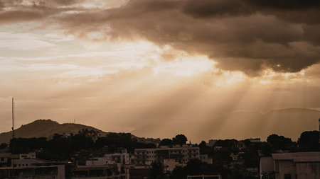 A serene sunset over a cityscape with rays of sunlight breaking through the clouds, illuminating the buildings below.の写真素材