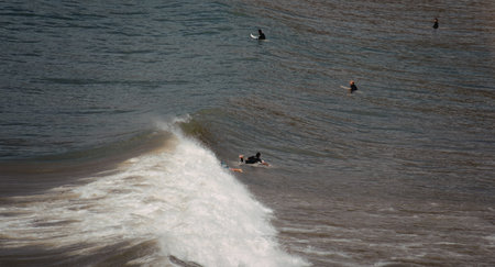 A surfer skillfully rides a wave in the ocean, with other surfers waiting in the background. The...