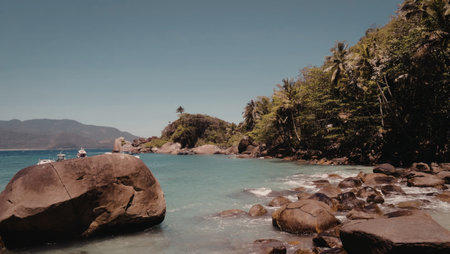 A serene tropical island with crystal clear turquoise waters, surrounded by rocky shores and lush green vegetation under a bright blue sky.の写真素材