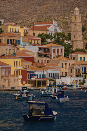 A picturesque coastal village featuring colorful buildings, a prominent clock tower, and several boats anchored in the clear blue water.の写真素材