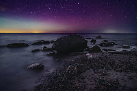 A captivating night scene featuring a rocky shoreline under a vivid sky filled with stars and colorful aurora lights.の写真素材