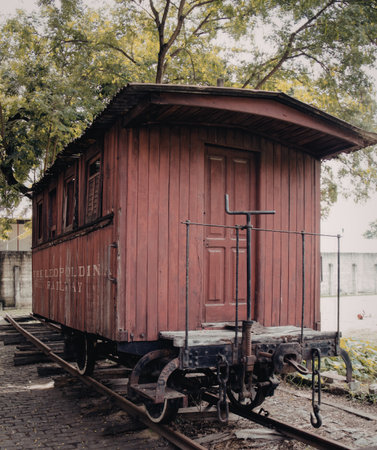 A red vintage railroad caboose is situated on train tracks, surrounded by lush green trees and vegetation. The caboose features wooden construction and classic design elements, indicative of historical railway transportation.の写真素材