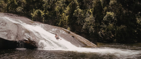 A picturesque waterfall cascades down a rocky cliff into a tranquil pool of water, surrounded by lush greenery.の写真素材