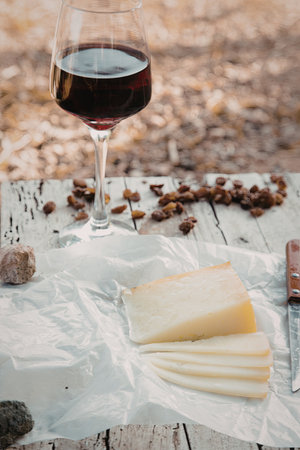 A close-up image of a wine glass filled with red wine, a wedge of cheese, and scattered nuts on a wooden surface.の写真素材