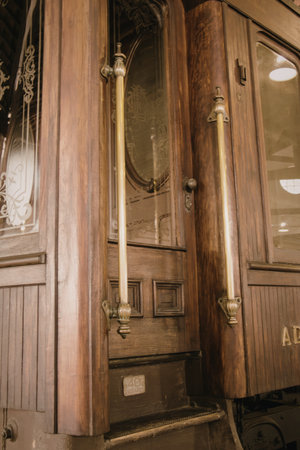 A close-up view of a vintage wooden door featuring ornate brass handles and glass panels. The door has intricate carvings and a classic design, indicative of historical architecture.の写真素材