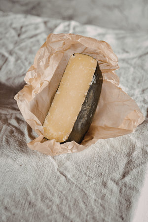 A piece of cheese wrapped in brown paper, placed on a textured cloth.