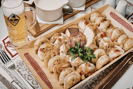 A wooden tray filled with dumplings, garnished with herbs, accompanied by a glass of beer and a...