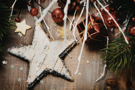 A close-up image of a wooden star ornament dusted with powdered sugar, surrounded by festive holiday decorations including red baubles, pine branches, and small star-shaped confetti.の写真素材