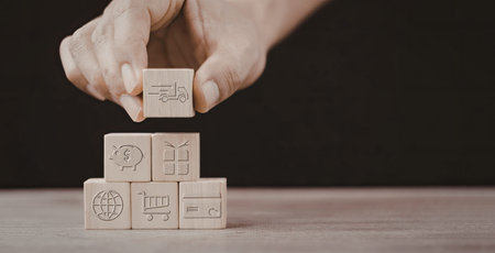 A hand placing a wooden block on top of a stack of other blocks, each block featuring different...