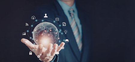 A businessman in a suit is holding a digital globe with various icons representing global...