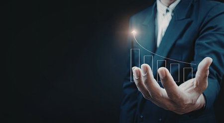 A businessman in a suit is holding a digital graph in his hand, symbolizing data analysis and business growth.の写真素材