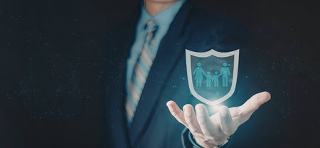 A businessman in a suit is holding a glowing protection shield that features a family silhouette, symbolizing security and protection.の写真素材