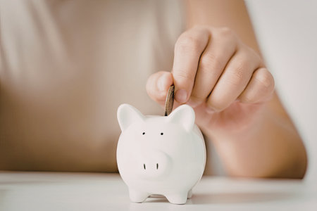 A young child is placing a coin into a white piggy bank, emphasizing the concept of saving money.の写真素材