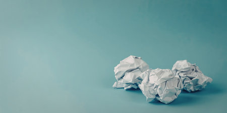 An image featuring several crumpled paper balls placed on a plain blue background. The simplicity of the scene emphasizes the texture and shape of the crumpled paper against the smooth, solid blue backdrop.の写真素材