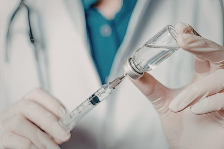 A healthcare professional in a white coat and gloves is carefully filling a syringe with a vaccine from a vial.の写真素材