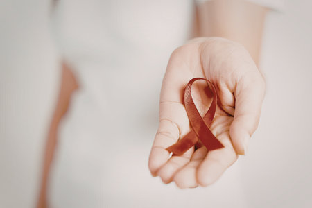 A close-up image of a hand holding a red ribbon, symbolizing awareness and support for a cause, likely related to health or social issues.の写真素材