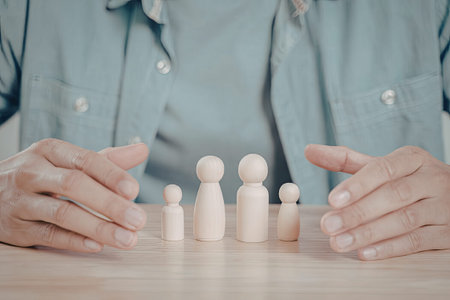 A close-up image of a person's hands carefully arranging a line of wooden figures on a table.