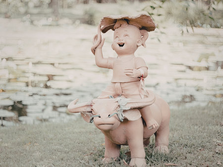 A joyful child in an outfit rides a statue in a lush park setting. The child is holding a hat and appears to be enjoying the experience.の写真素材