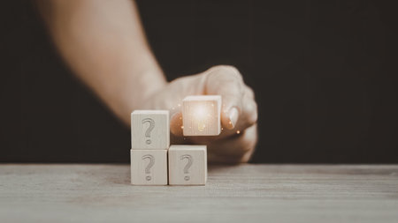 A close-up image of a hand holding a lit candle near three stacked blocks with question marks on them.の写真素材