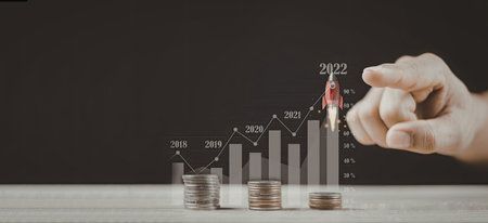 An image depicting a hand adjusting a financial growth chart over a stack of coins, with years...