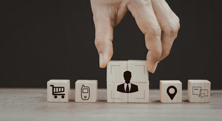 An image showing a hand adjusting a wooden block featuring a businessperson icon, surrounded by...