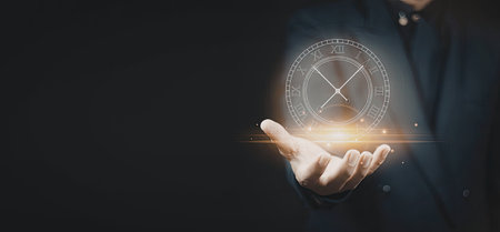 A person's hand holding a futuristic clock with a glowing effect against a dark background.の写真素材