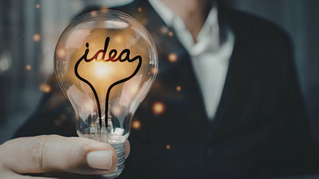 A person in a suit holding a light bulb with the word 'idea' illuminated inside, symbolizing...