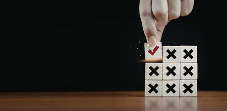 A close-up image of a hand selecting a check mark on a tic tac toe game board. The board features a mix of X and O symbols, with the check mark being the only symbol highlighted in red.の写真素材