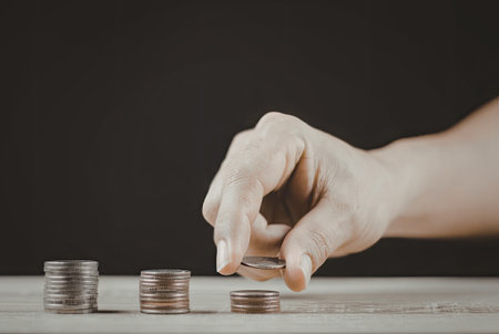 A close-up image of a hand stacking coins on a wooden surface, emphasizing financial planning and savings.の写真素材