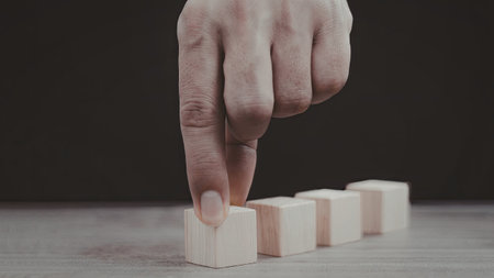 A close-up image of a hand carefully stacking wooden blocks in a row on a flat surface.の写真素材