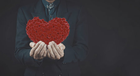A close-up image of a businessman in a dark suit holding a large red heart made of smaller red...
