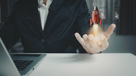 A businessman in a suit launching a red rocket from his hand, symbolizing innovation and success in a professional setting.の写真素材