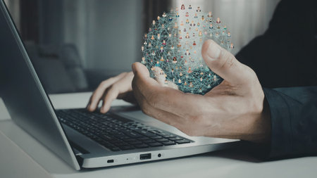 A person is holding a detailed globe model with pins while using a laptop on a desk. The image...