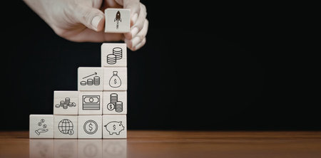 A hand is stacking white blocks, each featuring different icons. The blocks are arranged in a pyramid shape on a wooden surface.の写真素材