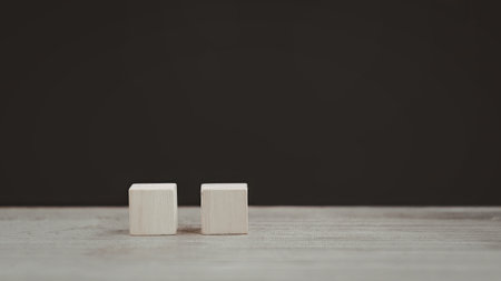 A minimalist image featuring two white cubes placed side by side on a plain, light-colored surface against a dark background.の写真素材