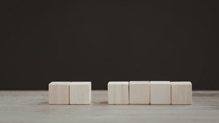The image features two stacks of light-colored wooden blocks placed on a plain concrete surface against a dark background.の写真素材