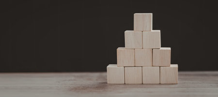 A collection of light-colored wooden blocks arranged in a pyramid shape against a dark background.の写真素材