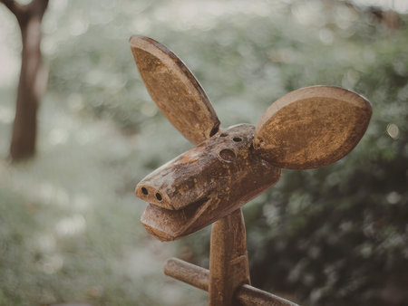 A rustic wooden deer head sculpture mounted on a wooden post in a lush garden setting. The sculpture features large antlers and is surrounded by greenery.の写真素材