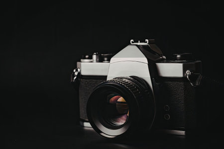 A vintage camera with a black and silver body is prominently displayed against a stark black background. The camera features a large lens and various dials and buttons, highlighting its classic design.の写真素材