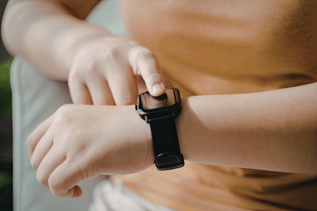 A close-up image of a child's hands adjusting a smartwatch on their wrist. The child is wearing a light-colored shirt and the smartwatch has a black strap and a digital screen.の写真素材