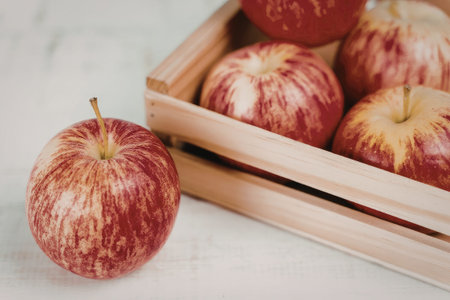 A close-up image of several fresh red apples, some placed in a wooden crate on a marble surface.の写真素材