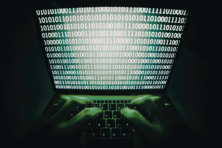 A close-up image of a laptop screen displaying binary code in green against a dark background. The screen shows a series of 1s and 0s, and the laptop keyboard is partially visible with green backlighting.の写真素材