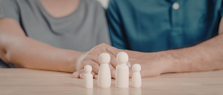 The image depicts a pair of hands carefully arranging a set of wooden figures on a wooden table. The figures are small and appear to be crafted from light-colored wood.の写真素材