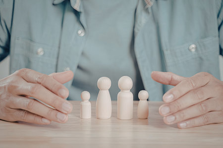 A close-up image of a person's hands carefully arranging a line of wooden figures on a table.の写真素材
