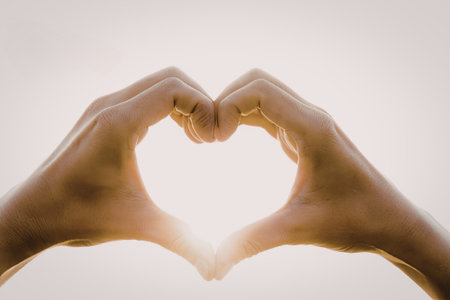 A pair of hands forming a heart shape with sunlight shining through, creating a warm and loving atmosphere.の写真素材