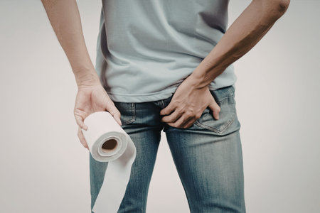 A person wearing a light blue t-shirt and blue jeans is holding a roll of toilet paper with one hand...